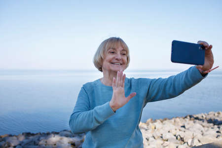 Happy senior woman talking to her family via video call during traveling to sea, active retirement, social distance, silver surfers, healthy lifestyleの写真素材
