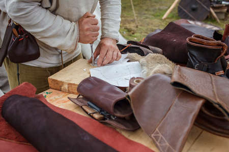 Craft shoemaker demonstrates the process and the products of his work on the festival workshop, tools and leather at cobbler workplace, diy, master of artisanal thing, middle age re-enactmentの写真素材