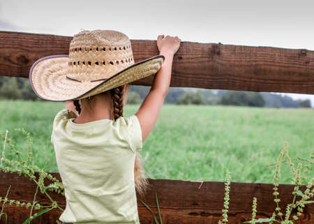 Local vacation, stay safe, stay home. Little girl in cowboy hat playing in western in the farm among...