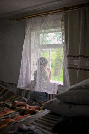 Cute child opening a window for fresh air in the early morning in the village home, happy...