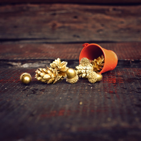 Golden pine cones and acorns pouring out of tiny orange bucket on the rural wooden background, autumnal harvest, trendy golden fall season conceptの写真素材