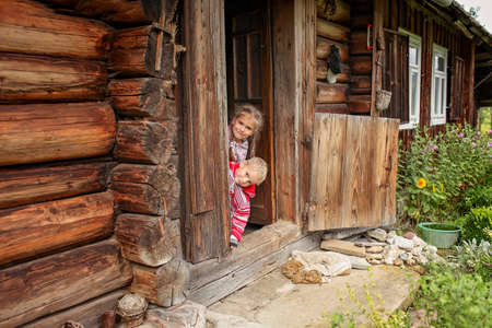 Happy boy and girl having fun and rest together on the doorstep of old wooden house during summer vacation, eco-friendly travel concept, outdoor summertime lifestyleの写真素材