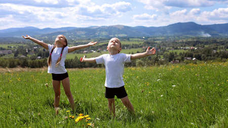 Two cute sibling doing their morning exercises on the top of the mountains in summer nature, morning exercises, sport and healthy lifestyle, outsideの写真素材