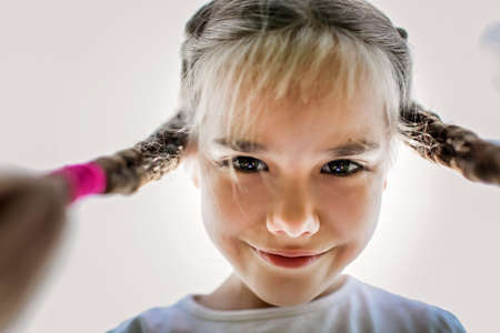 Close-up candid portrait of cute 7-8 years old girl with two funny braids taken up at the sky from the ground, happy summertime, outdoor lifestyleの写真素材