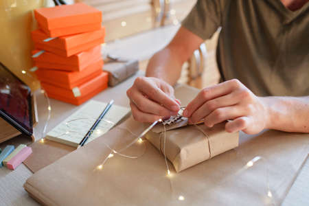 Hands of young millennial worker packing Christmas gift boxes for clients, family small business. New Year celebration, distant work and home office, indoor lifestyleの写真素材
