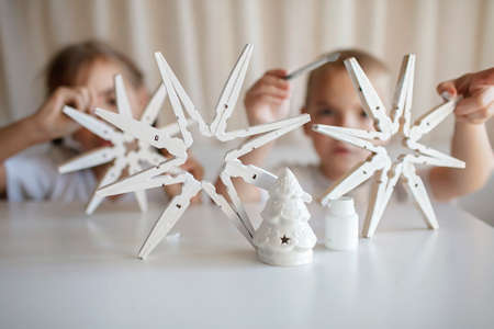 Siblings, boy and girl, paint wooden snowflakes from clothespins with white paint at home, hands in paint, recyclable craft ornament, New Year DIY decoration, selective focus on snowflakeの写真素材