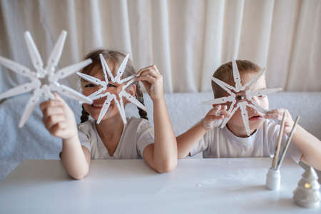 Two kids, sister and brother sitting before crafted Christmas snowflakes from wooden clothespin, reusable original ornament, DIY New Year decoration, handmade home children activityの写真素材