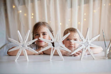 Two kids, sister and brother sitting before crafted Christmas snowflakes from wooden clothespin, reusable original ornament, DIY New Year decoration, handmade home children activityの写真素材