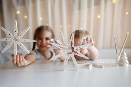 Two kids, sister and brother sitting before crafted Christmas snowflakes from wooden clothespin, reusable original ornament, DIY New Year decoration, selective focus on snowflakeの写真素材