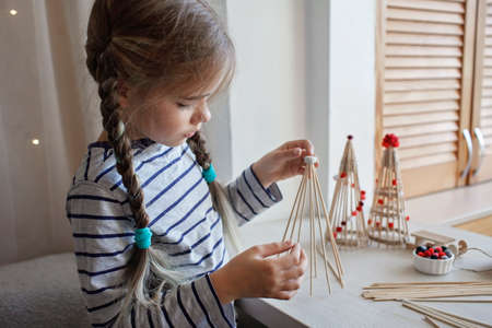 Girl makes wooden crafted Christmas tree from bamboo marshmallow roasting sticks at home, recyclable craft ornament, New Year DIY decorationの写真素材