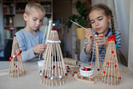 Two kids, sister and brother, make crafted Christmas tree from bamboo marshmallow roasting sticks, reusable original ornament, DIY New Year decoration, selective focus on decorの写真素材