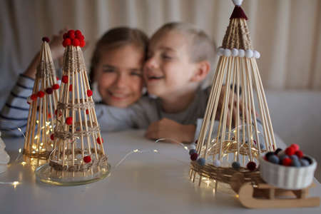 Siblings, boy and girl, sitting and dreaming before crafted Christmas tree from bamboo sticks, magical lights, reusable original ornament, DIY New Year decoration, selective focus on treesの写真素材