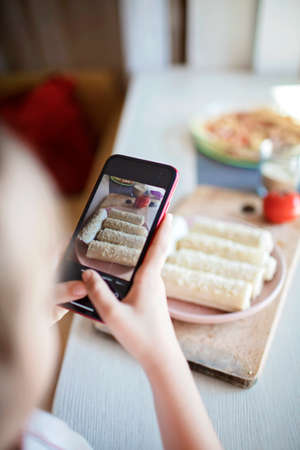 Cute girl takes photo of sausage rolled in phyllo pastry to share it for her mom in social media. Tasty snack for kids, filo dough pastry, little chef enjoys cooking at homeの写真素材