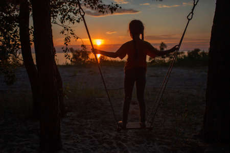 Happy girl swinging and looking at sunset by the sea in autumn, family walking in nature, fall vibes, travel and active lifestyle concept, golden hoursの写真素材