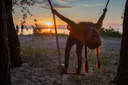 Happy girl having fun at swing at sunset by the sea in autumn, family walking in nature, fall vibes, travel and active lifestyle concept, golden hoursの写真素材