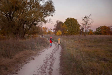 Two siblings run along a country road after their dad while walking in beautiful autumn forest. Warm weather and warm stories, outdoor lifestyle, active family lifestyle.の写真素材