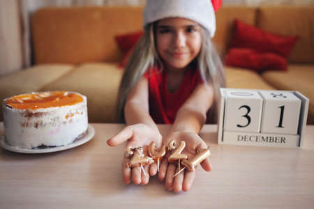 Happy girl in Santa hat shows burnt candles of numbers 2021 in her palms as a symbol of outgoing year, last day of December, Christmas cake is ready, family New Year celebration, focus on candlesの写真素材