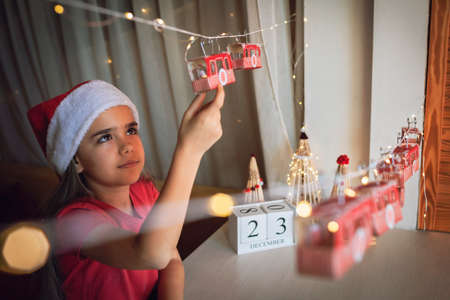 Happy kid opens crafted advent calendar on theme of skis and cable car. Ski resort funicular of rolls from toilette paper. Zero waste and reusable Christmas. Magic winter holiday, focus on girlの写真素材