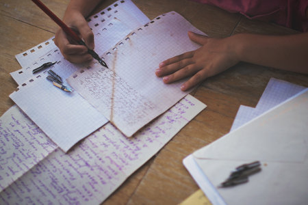 A little girl writing a letter with ink pen, old envelopes, ink pen and set of replacement pens on...