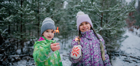 Happy kids with burning sparklers during walking in forest on snowing day, outdoor family Christmas celebration, excited family in warm clothesの写真素材