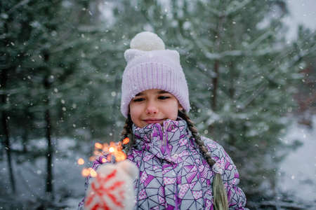 Happy kids with burning sparklers during walking in forest on snowing day, outdoor family Christmas celebration, excited family in warm clothesの写真素材