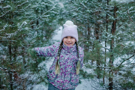 Pretty girl in warm clothes, with frozen mittens enjoys the first long-awaited snow during family walking in forest on snowing day, outdoor lifestyle, winter wonderlandの写真素材