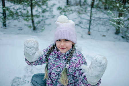 Pretty girl in warm clothes shows her frozen mittens and enjoys the first long-awaited snow during family walking in forest on snowing day, outdoor lifestyle, winter wonderlandの写真素材