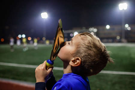 Young soccer player in blue jersey with ten number kissing a winners cup after the winning goal in the football tournament, illuminated stadium, sport, winner and success. Dreams come trueの写真素材