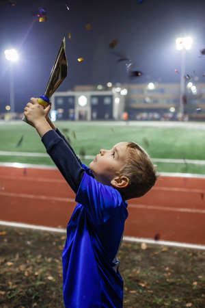 Young soccer player in blue jersey with ten number holding a winners cup after the winning goal in the football championship, illuminated stadium, sport, winner and success. Dreams come trueの写真素材