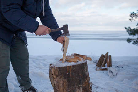 Family winter picnic. Dad chops wood for a fire on the shore of a frozen lake during a winter family...
