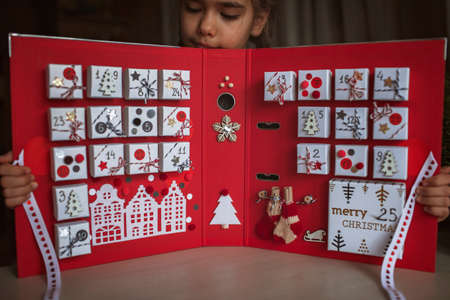 Pretty girl holds an original advent calendar made of jewelry boxes and a binder, New Year craft,...