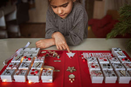 Pretty girl looks at original advent calendar made of jewelry boxes and a binder, New Year craft,...