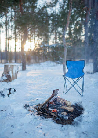 Family winter picnic. Bonfire and camping chair, winter family walk in snowy forest, outdoor weekend at snowing day, winter travel, vertical photoの写真素材