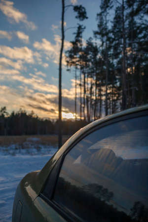 A part of car in snowy pine forest on sunset, gorgeous winter landscape, background with copy space, winter road trip, silence and wild nature, travel in any season, vertical photoの写真素材