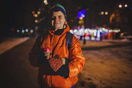 Happy middle aged man holding a gift with crafted heart to give to his love partner at Valentine Day or Christmas, authentic lifestyle in winter cityの写真素材