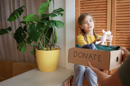 Mother with daughter sort out the wardrobe and collect clothes and toys for donate box at home. Second hand and circular fashion activism, sustainable consumerism.の写真素材