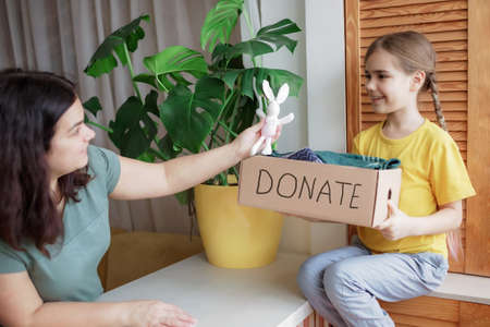 Mother with daughter sort out the wardrobe and collect clothes and toys for donate box at home. Second hand and circular fashion activism, sustainable consumerism.の写真素材