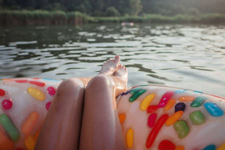 A smiling tween girl relaxing on a big donut shaped inflatable ring on a lake on a hot summer day, happy summertime in countryside, local vacations, cottagecoreの写真素材