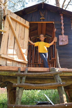 Thoughtful pretty girl is in beautiful creative handmade treehouse in backyard, summer activity, cottagecore, happy summertime in countryside, ecological outdoor playgroundの写真素材
