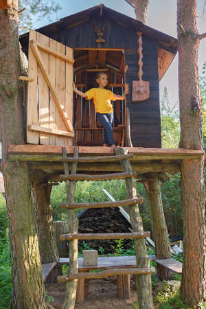 Thoughtful pretty girl is in beautiful creative handmade treehouse in backyard, summer activity, cottagecore, happy summertime in countryside, ecological outdoor playgroundの写真素材