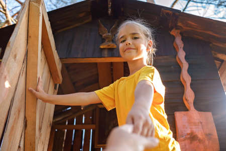 Pretty girl invites in beautiful creative handmade treehouse in backyard, summer activity, cottagecore, happy summertime in countryside, ecological outdoor playgroundの写真素材