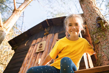 Happy pretty girl looking down from the beautiful creative handmade treehouse in backyard, summer activity, cottagecore, happy summertime in countryside, ecological outdoor playground, lower angleの写真素材
