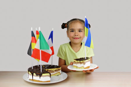 Girl holds baked cake with several European flags in it, Ukrainian flag on the separate part. One...