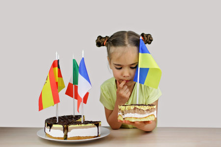 Girl holds baked cake with several European flags in it, Ukrainian flag on the separate part. One piece and one peace. Europe and euro integration way, studio shot, isolated over grey backgroundの写真素材