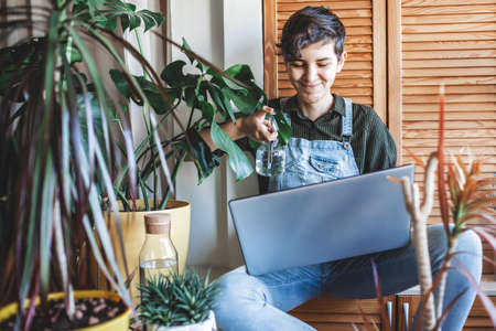 Happy young girl with laptop surrounded by home plants on the balcony, online communication, plant influencer, home gardening, green decor and environment at home, generation Z trendの写真素材
