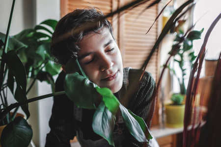 Portrait of happy young girl with closed eyes among home plants on the balcony, plant parent concept, home gardening, green decor and environment at homeの写真素材