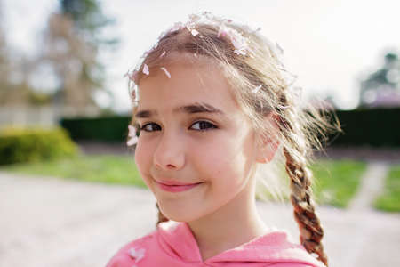 Emotional portrait of happy girl in a pink hoodie with sakura petals on her head and eyelashes that fell from trees when the wind blew. She rejoices in the coming of springtime. Spring vibes.の写真素材
