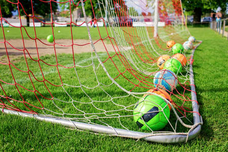 Many soccer balls in the net gate, equipment on green grass prepared for training in kids football academy. Health and active lifestyle. Popular sport activityの写真素材