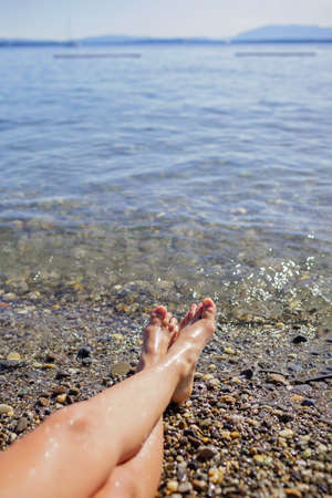 Female legs, a girl is sunbathing on a pebble beach on the shores of Geneva Lake, blue mountains in sun light, daydreaming and happiness, summer vacations, travel and summertime, lifestyleの写真素材