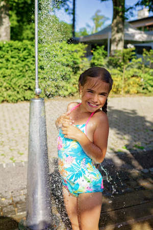 Pretty girl takes shower on the beach in the summer camp, refreshing in cold water, enjoying summer vacation on the sea resort, family travel and recreationの写真素材